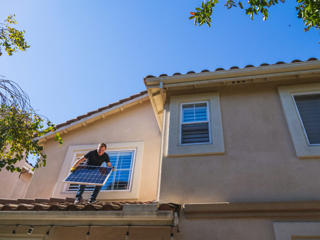 A man standing on the roof while holding a solar panel