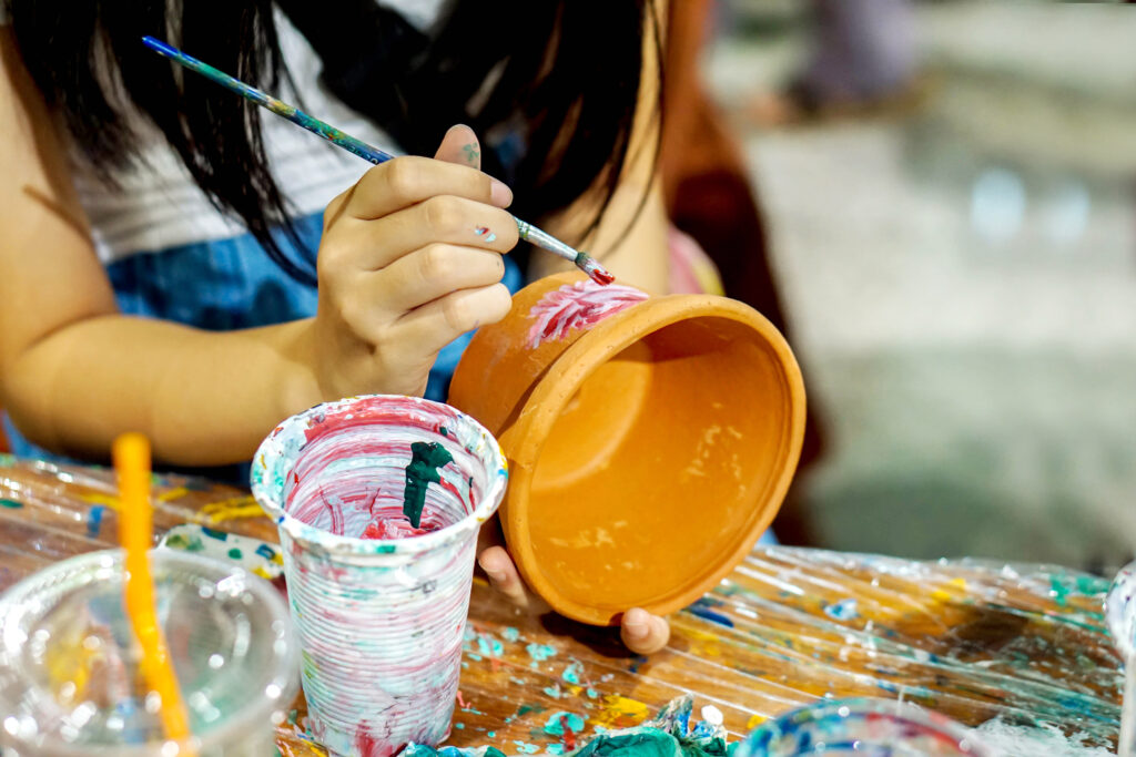 Asian little girl study and learning paint on flower pot in the art classroom of her school.