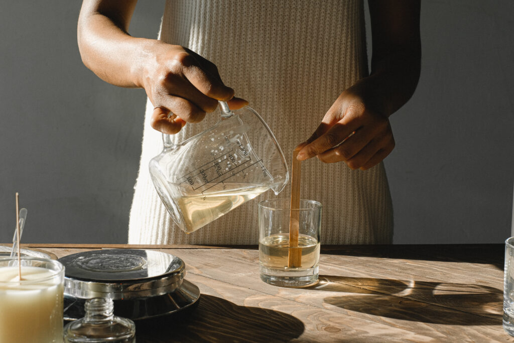 Crop black woman pouring wax into candle mold