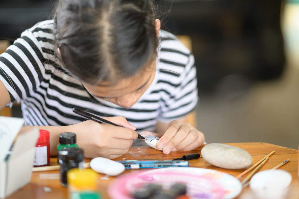 Cropped shot of young girl artist painting with water colour on rock.