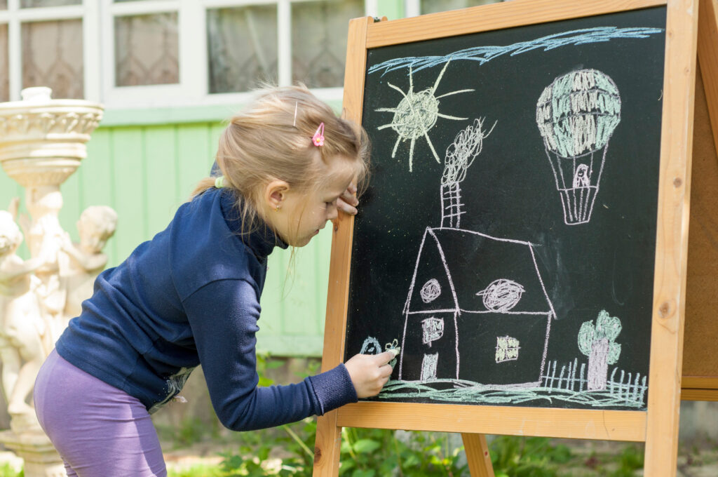 Little girl is drawing with chalk on a blackboard