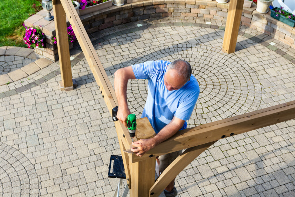 Man building a wooden gazebo on a brick patio