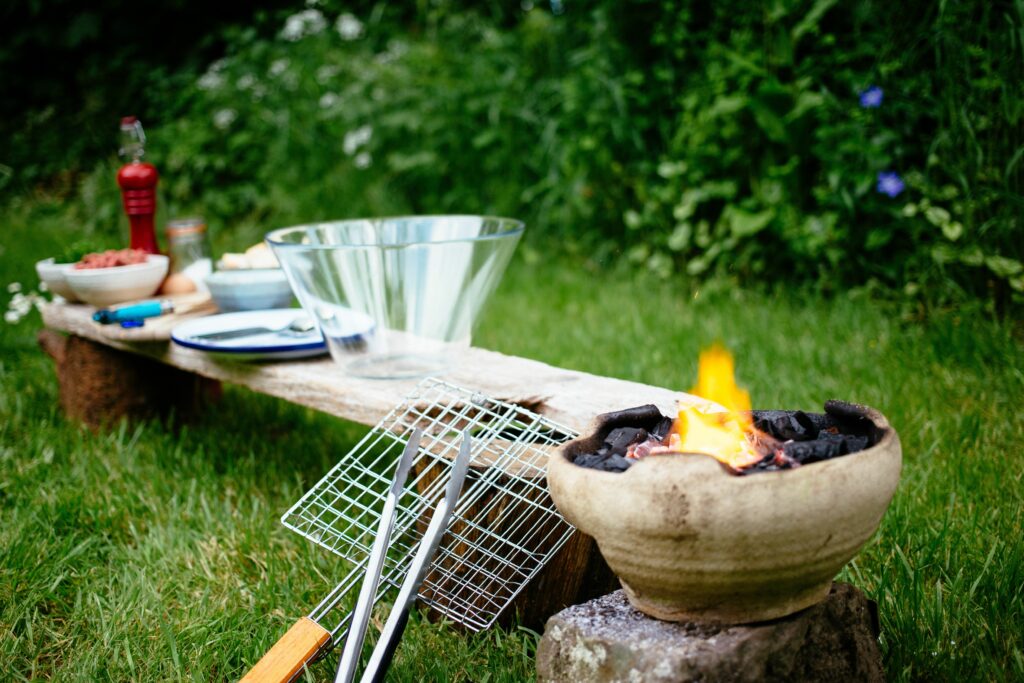 Small fire pit with the background of ingredients on a wooden board on wood stumps on the grass