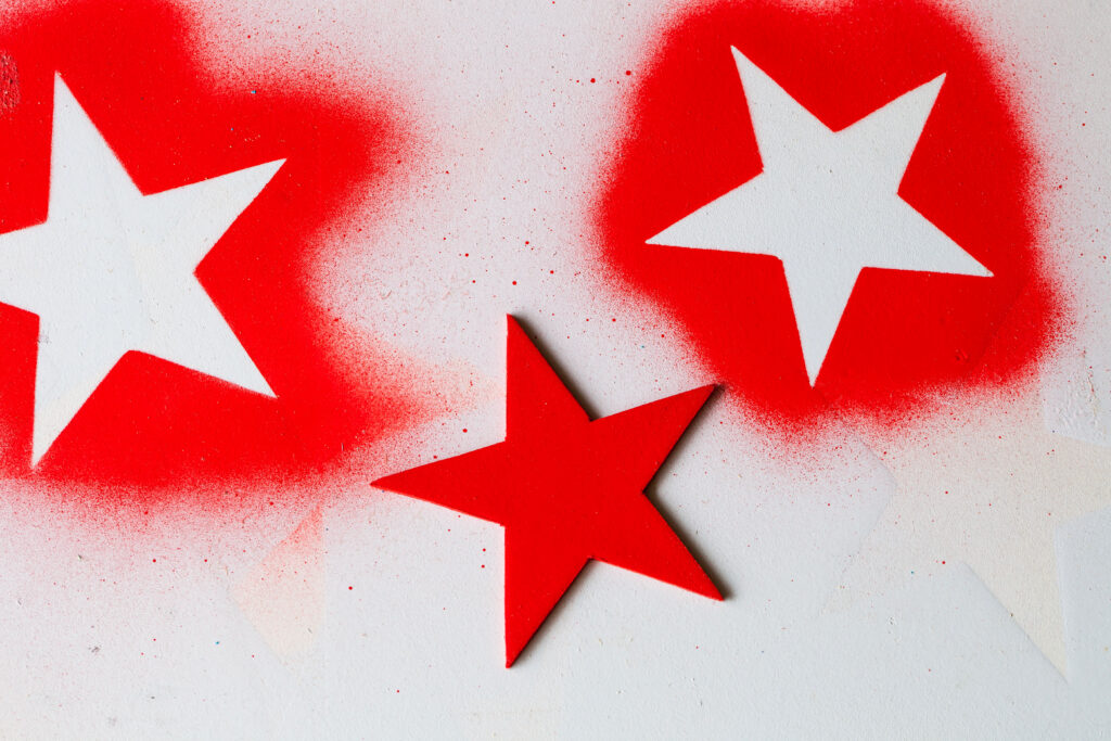 Textured background with white star shapes on red paint with red splatter and wooden red star