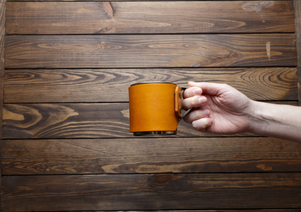 the girl is holding a mug. Stainless steel mug with insulated leather sleeve. travel mug on wooden background.