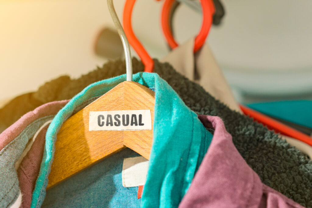 The word ' Casual ' on a paper label on wooden coat hanger. Clothes for men. Wardrobe. Dressing room. Male's shirts. Everyday outfit. Fashion. Job. Work. Street style. Boy. Guy. Stylish