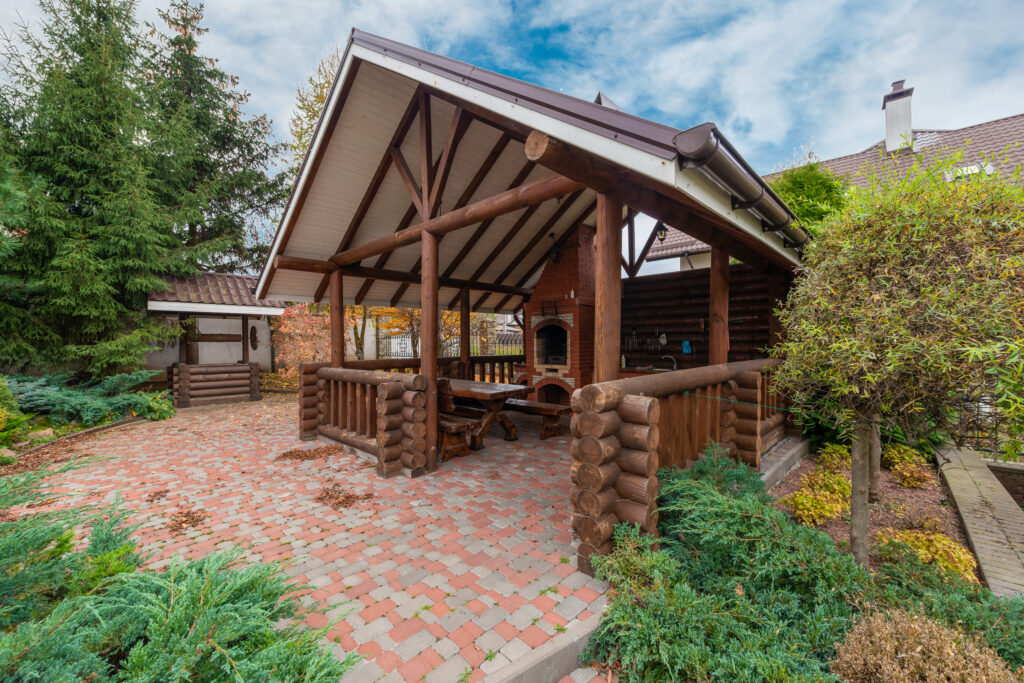 Wooden fence and roof over a grill and a table with chairs in a garden