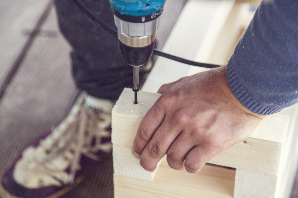 Crop unrecognizable workman drilling hole with nail in wooden plank