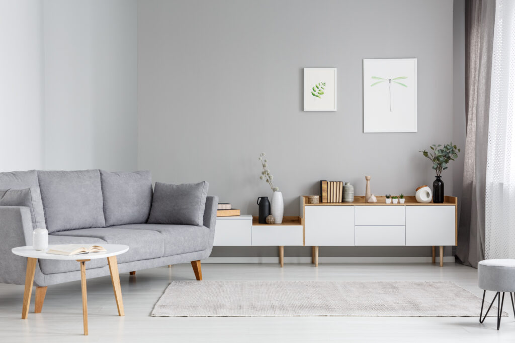 Grey settee near white cupboard in minimal living room interior with posters on the wall. Real photo