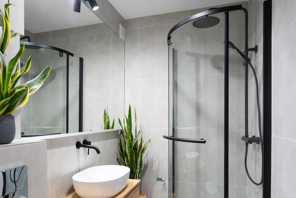 Interior of bathroom with shower, stylish wash basin and tap and mirror. Grey tiles and plants in spa at home.