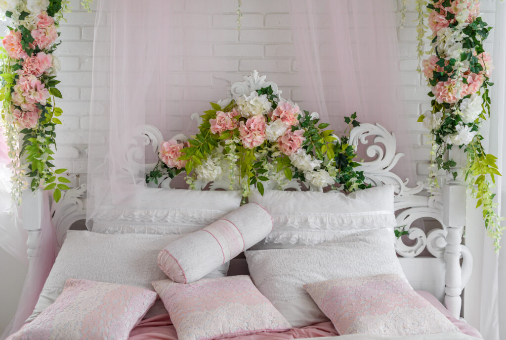 Large white wood bed with decorative headboard and white and pink pillows on it. Feminine bedroom in pink and white colors with brick wall and white bed, copy space