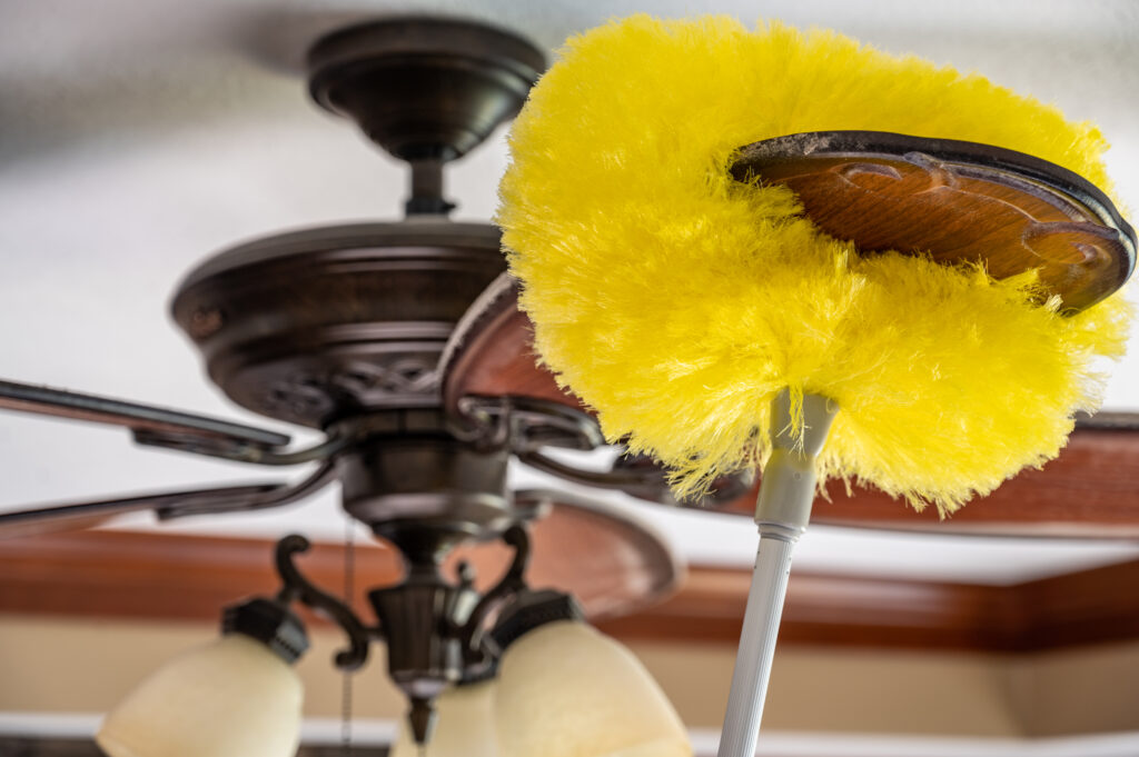 Using a wand feather duster to remove and clean dust from a ceiling fan