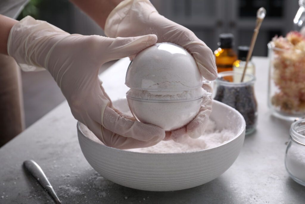 Woman in gloves making bath bomb at grey table, closeup