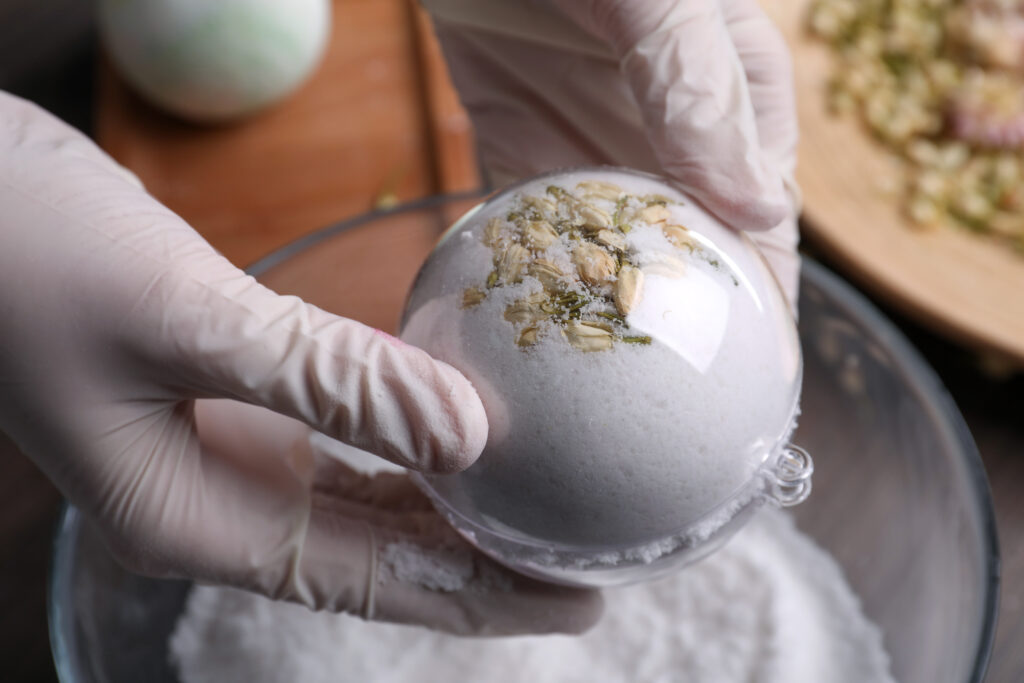 Woman in gloves making bath bomb at table, closeup