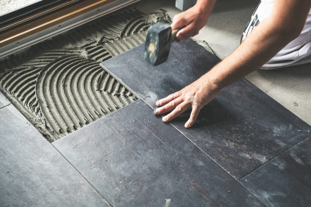 Worker placing anthracite ceramic floor tiles on adhesive surface. Construction labor, craftsmanship conceptual background.