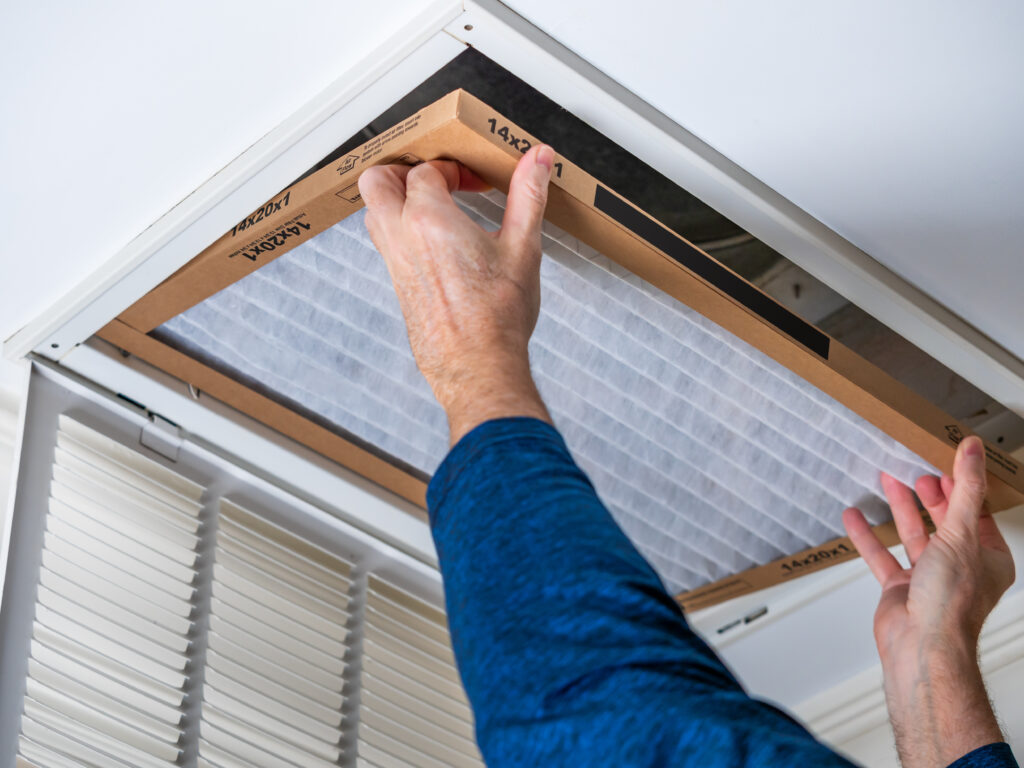 Man replacing dirty HVAC air filter in ceiling vent. Home air duct system maintenance for clean air.