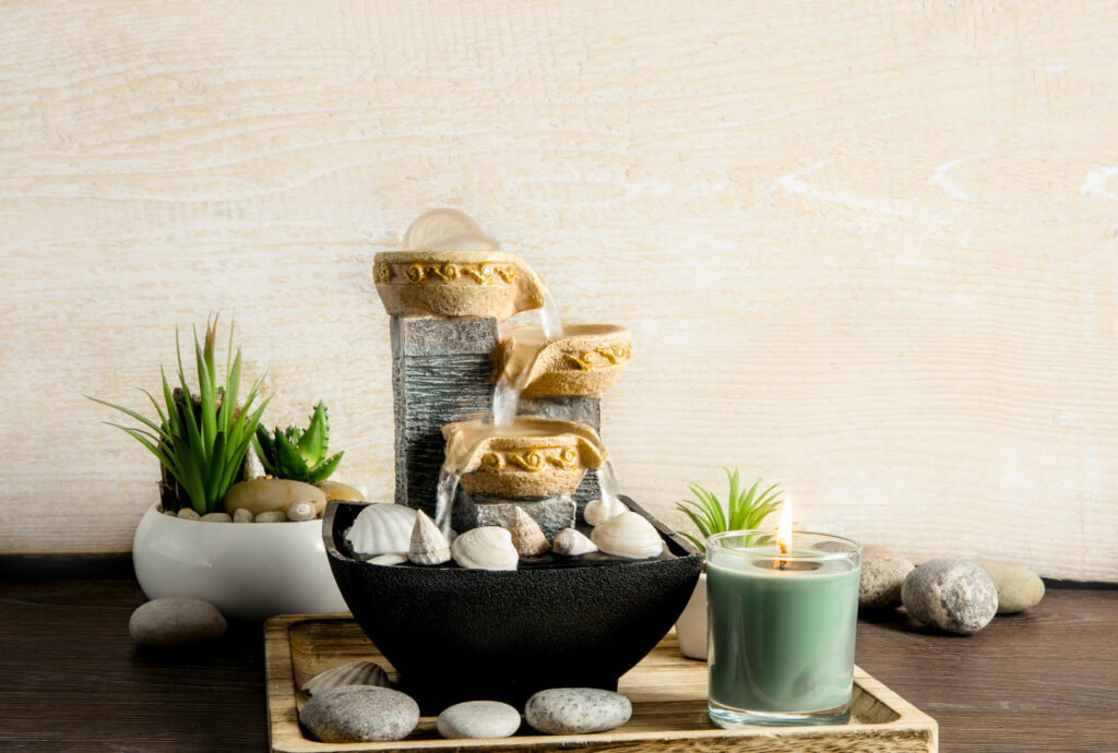 Portable indoor fountain for good Feng Shui in home or office. Small indoor tabletop fountain with water flowing. Spiritual mind and soul balance concept. Green plants in flower pot on background.