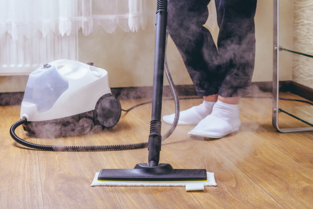 The woman washes the floor in the room with a white steam cleaner, a wet high-pressure steam. Cleaning of the apartment. we kill microbes