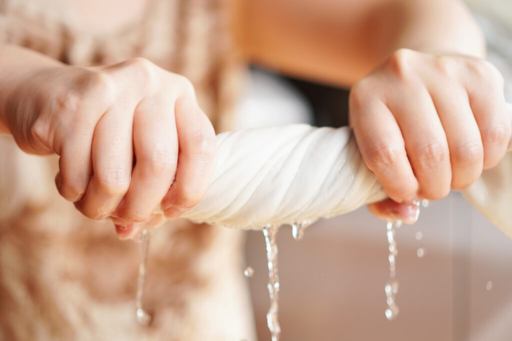 Two woman hands wring wet cloth after washing by twist and squeeze. Housework ,laundry and optimization concept ,selective focus on hand on the left