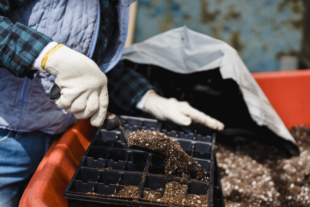 Unrecognizable gardener pouring soil into container