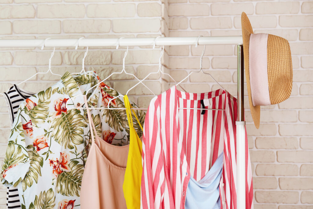 Women's hip clothing store interior concept. Row of different colorful female clothes hanging on rack in hipster fashion show room in shopping mall. White brick wall background. Copy space.