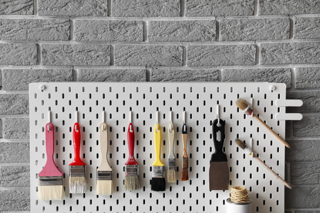Pegboard with decorator's tools on grey brick wall, closeup