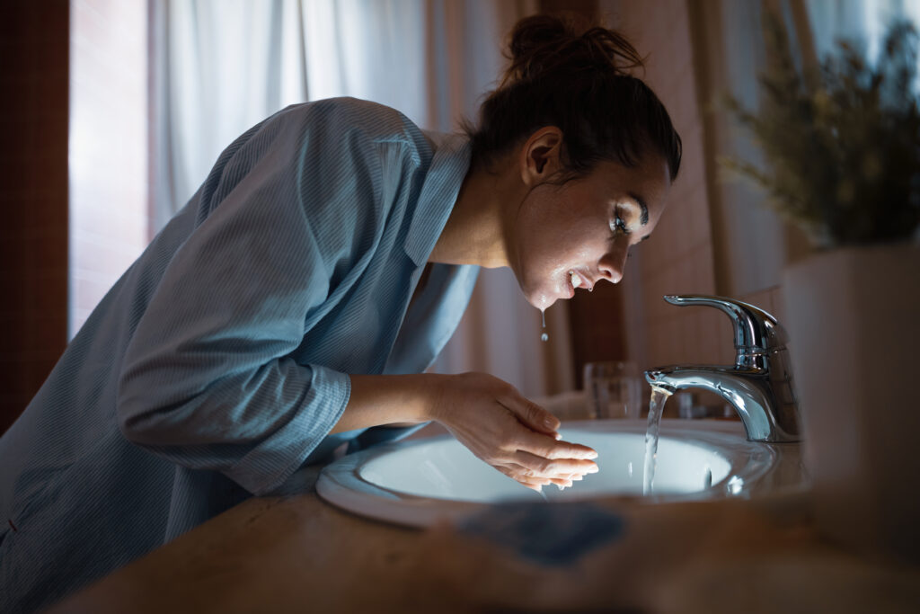 Young woman cleaning her face with water in the bathroom.