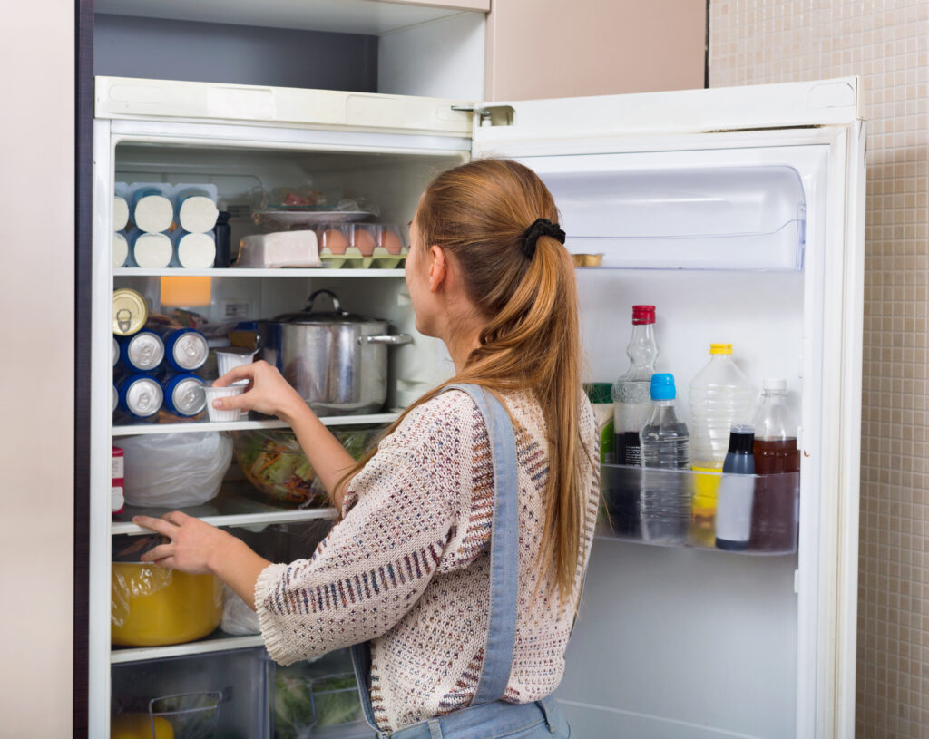 Accurate and smiling  girl standing near fridge