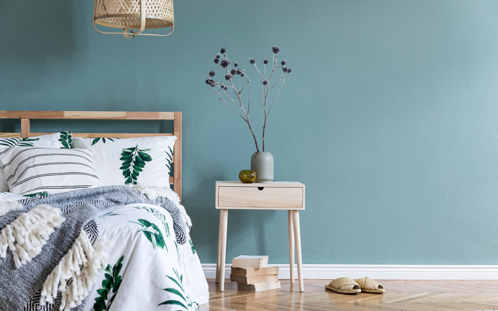 Minimalistic composition of bedroom interior with wooden bed, shelf, flowers in vase, rattan lamp, books and elegant accessories.