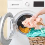 a person is putting clothes in a basket next to a washing machine