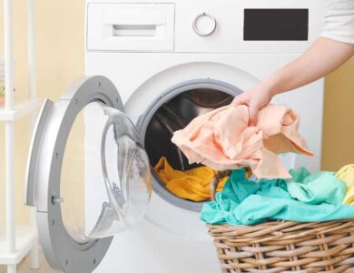 a person is putting clothes in a basket next to a washing machine