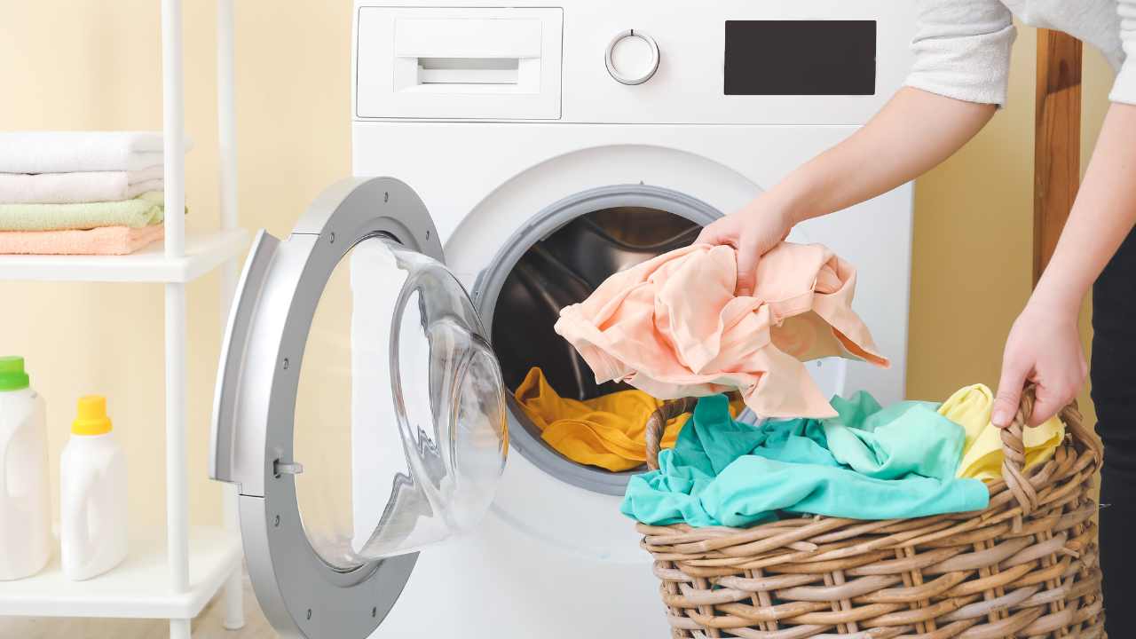 a person is putting clothes in a basket next to a washing machine