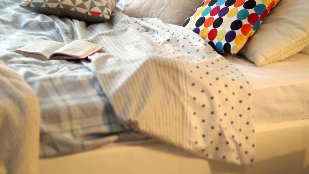 an unmade bed with pillows and a book on it