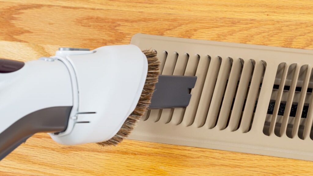 a person using a vacuum cleaner to clean a floor vent