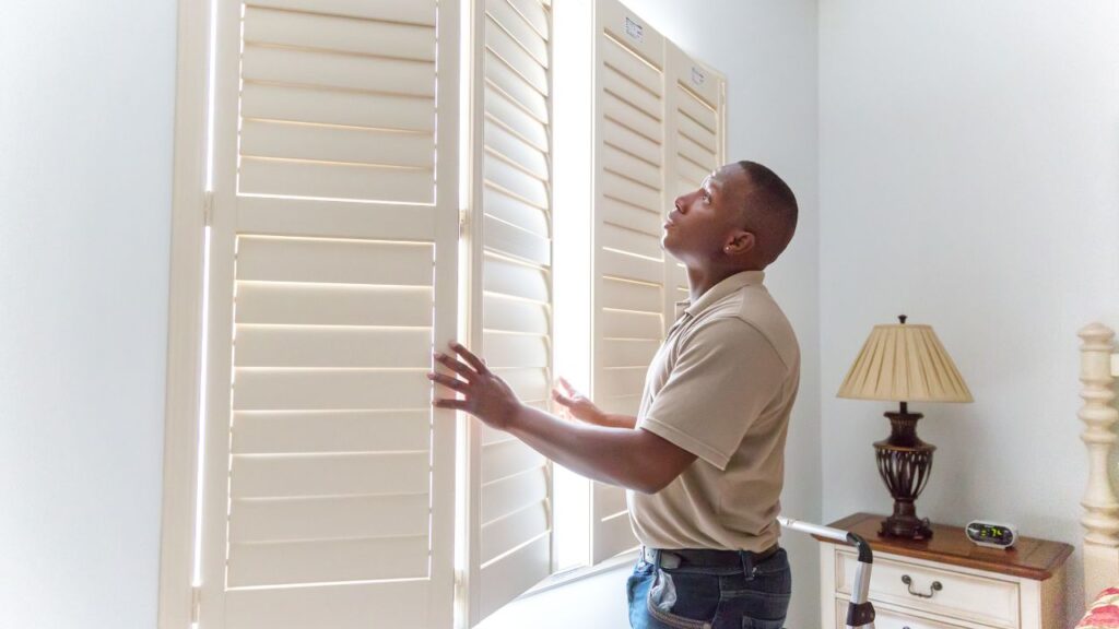 a person standing in front of a window with white shutters