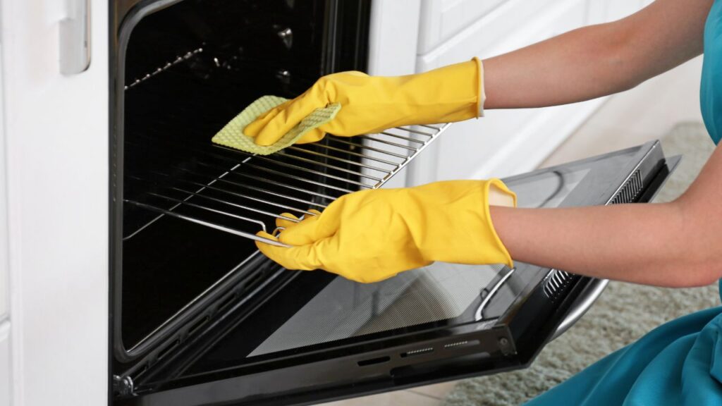 A person wearing yellow gloves is cleaning an oven