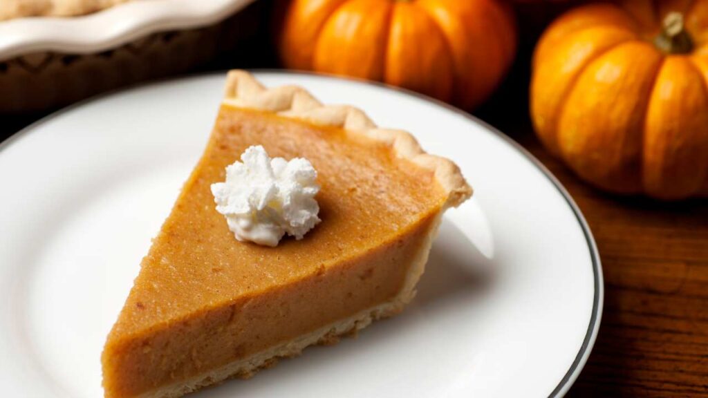 a slice of pumpkin pie sits on a plate next to pumpkins