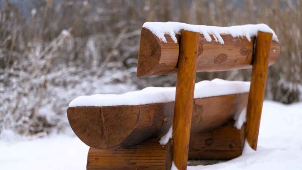 a wooden bench covered in snow sits in the middle of a snowy field