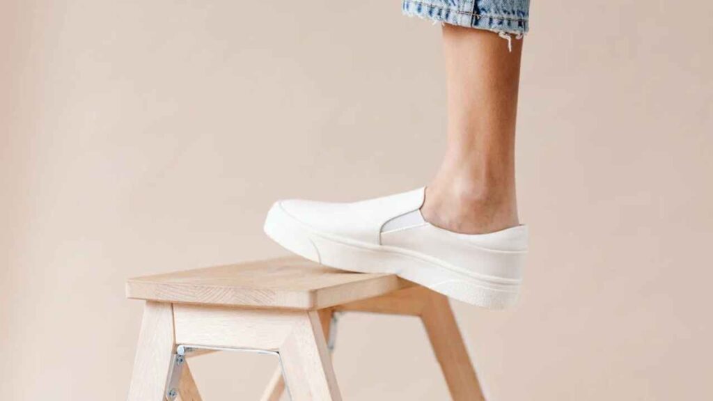 a person standing on a wooden stool wearing white sneakers