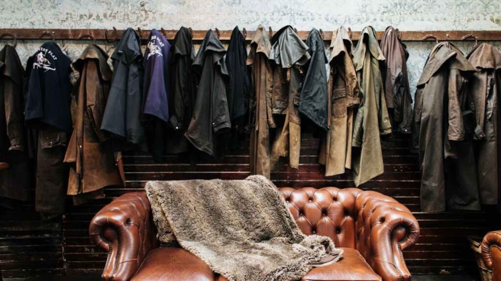 an old leather chair sits in front of a rack of coats