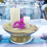 a glass vase filled with sand and flowers on a table