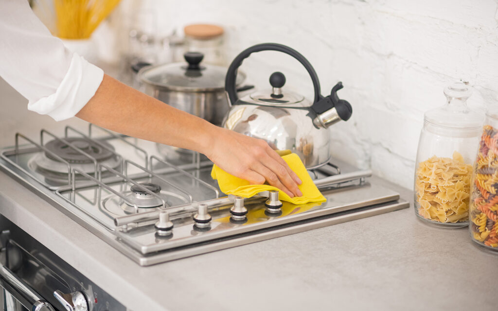 Woman cleaning cooking range with a microfiber cloth.